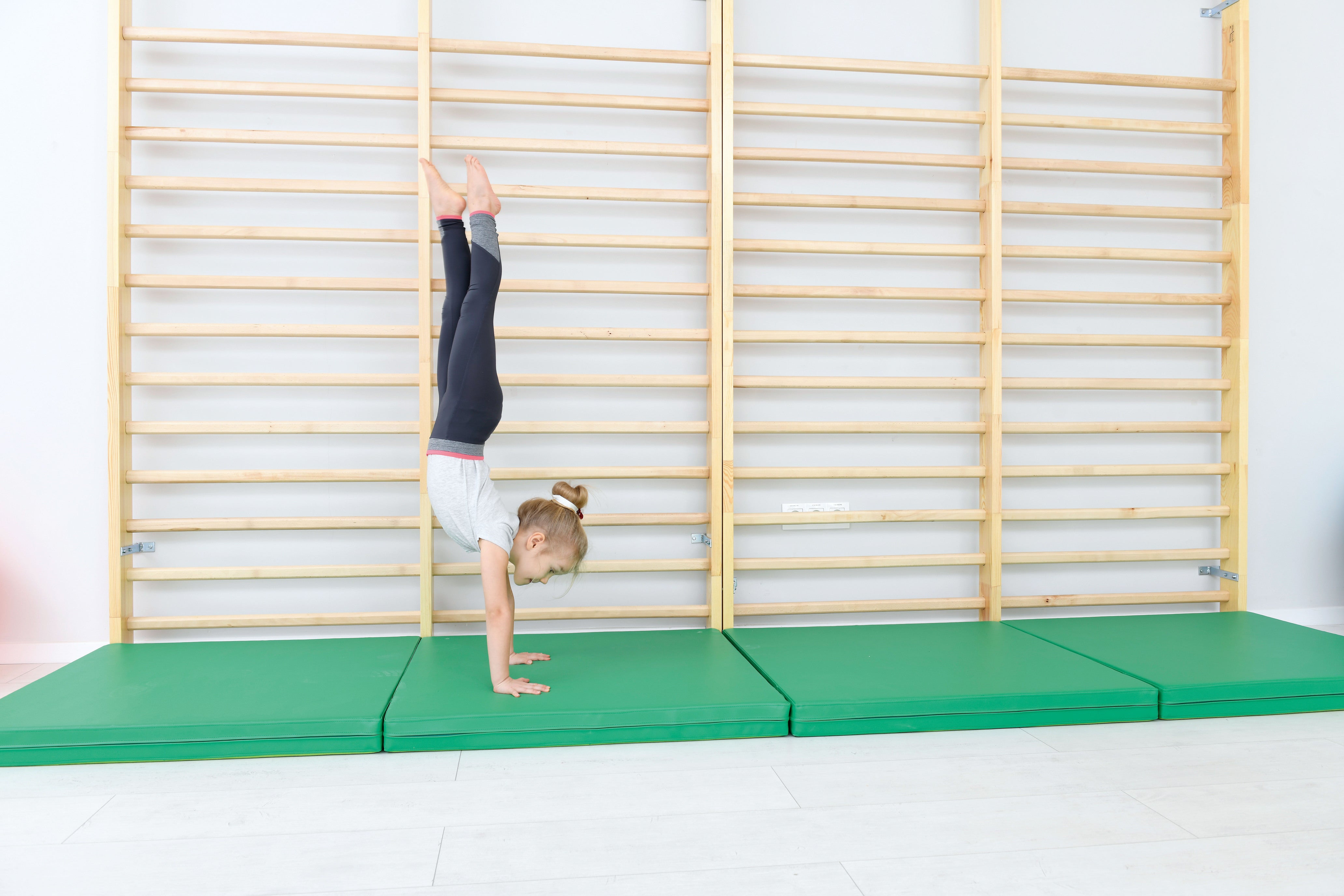 Fallschutzmatte für Kindergarten. Kind an Sprossenwand macht Handstand.