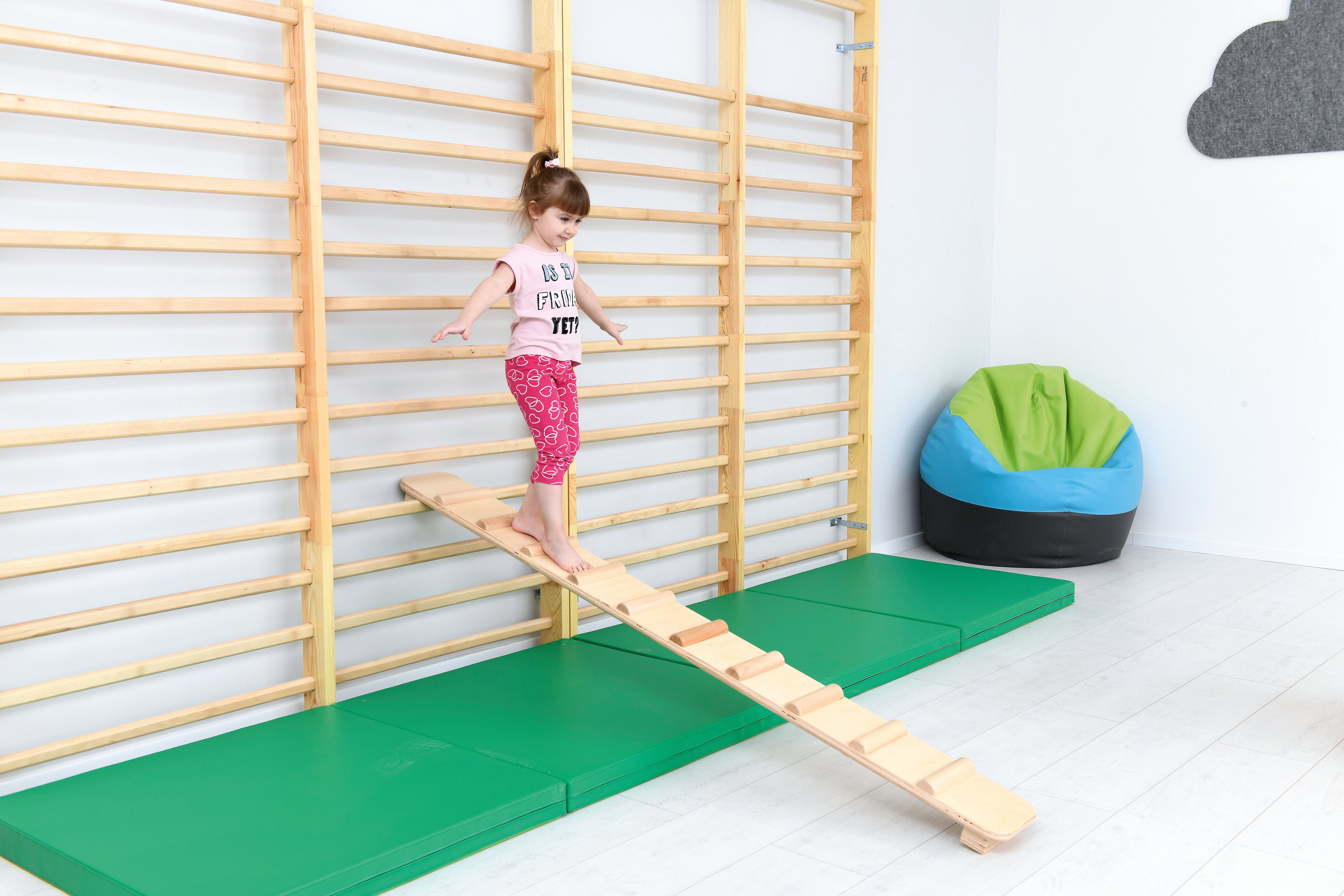 Fallschutzmatte für Kindergarten an Sprossenwand. Kind balanciert.