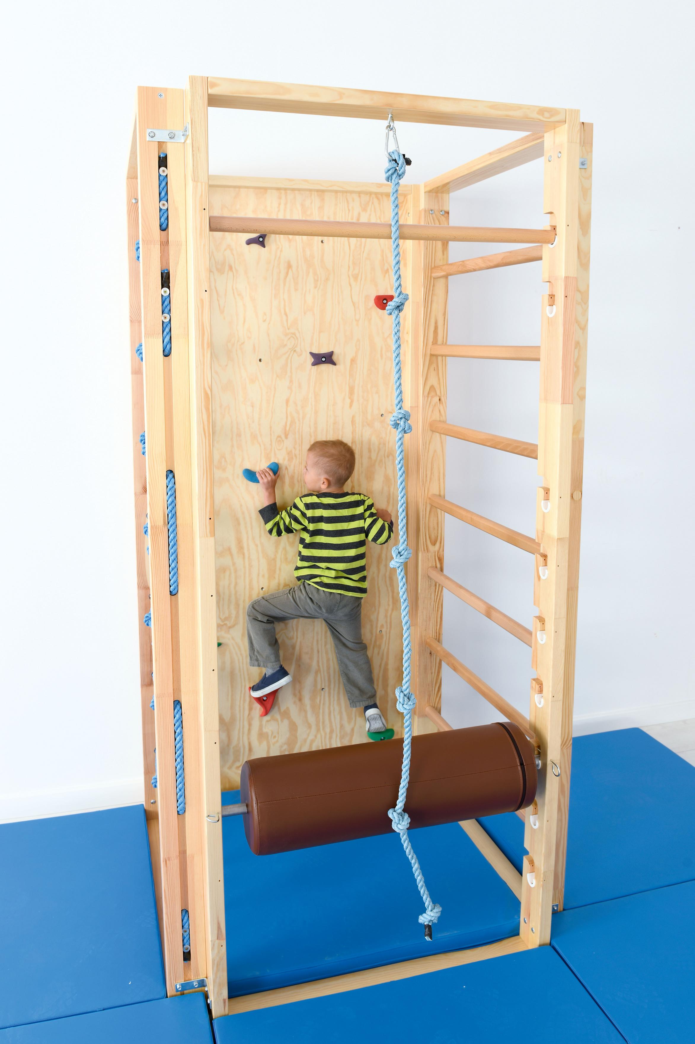 Kind auf Kletterwand in Turnhalle, fördert Bewegung.