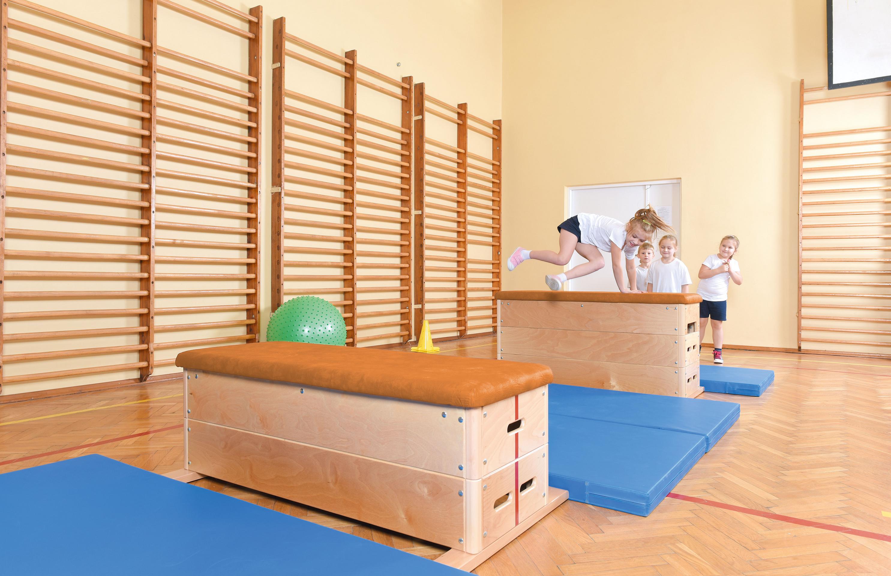 Kinder beim Spielen auf Sprungkasten in Turnhalle.