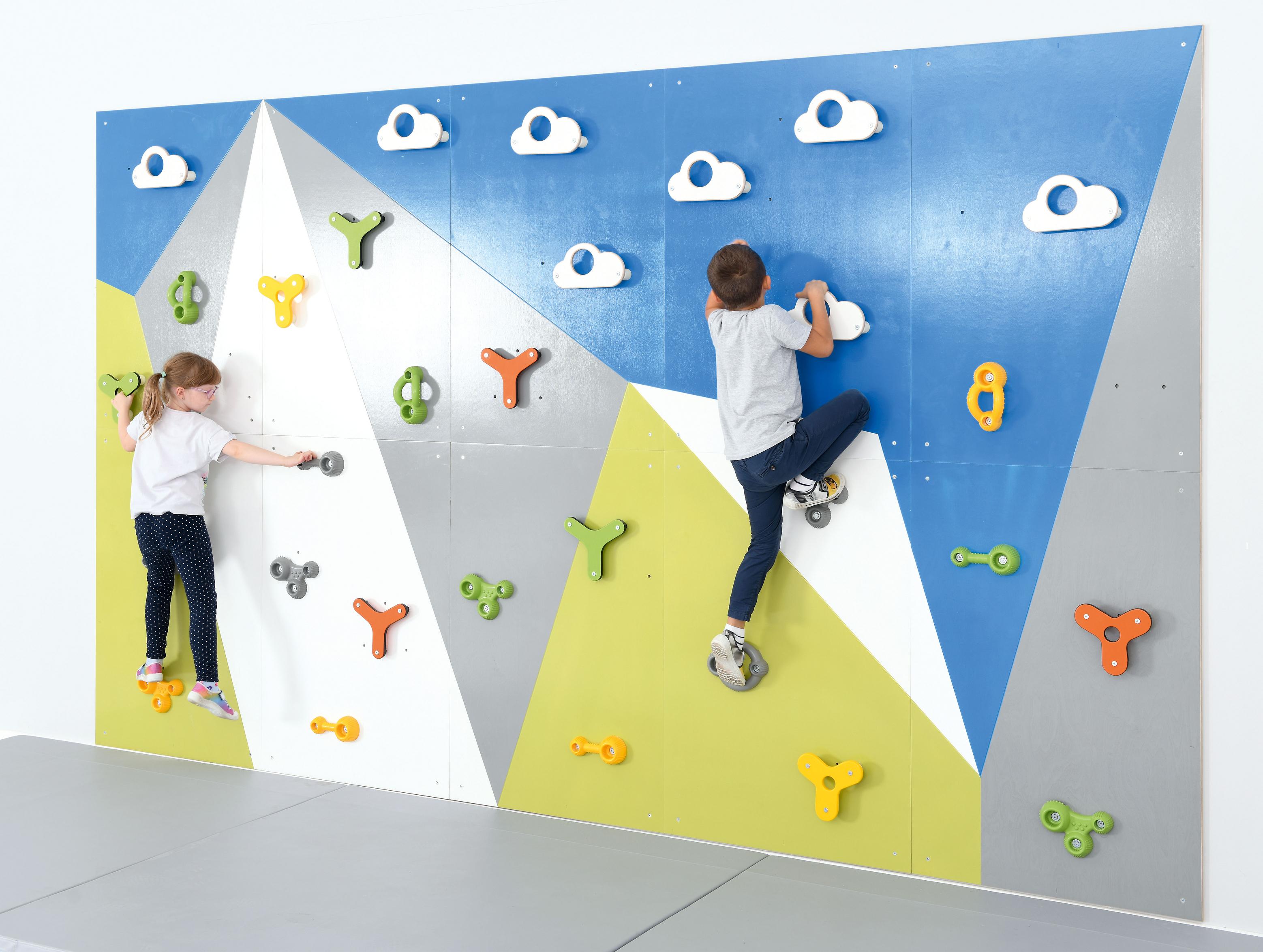 Kinder klettern auf bunte Kletterwand in Sporthalle.